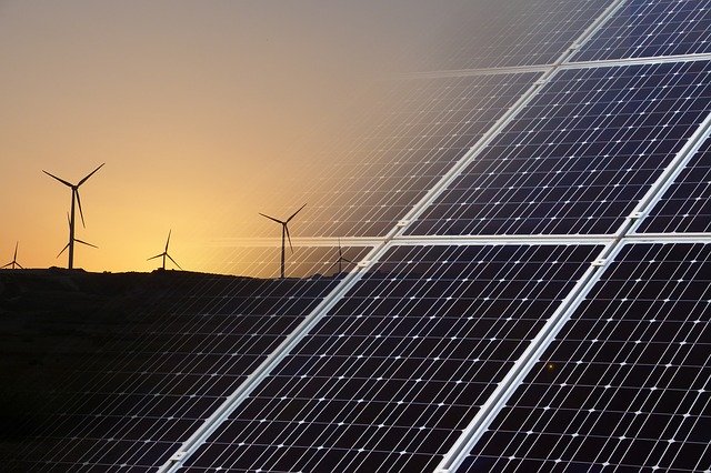 A combination of wind turbines and solar panels under a clear blue sky