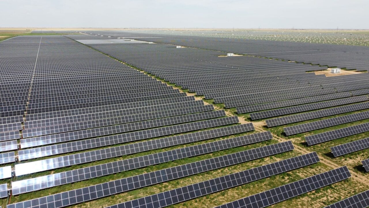 Large scale utility solar farm with integrated battery storage containers under a clear sky.