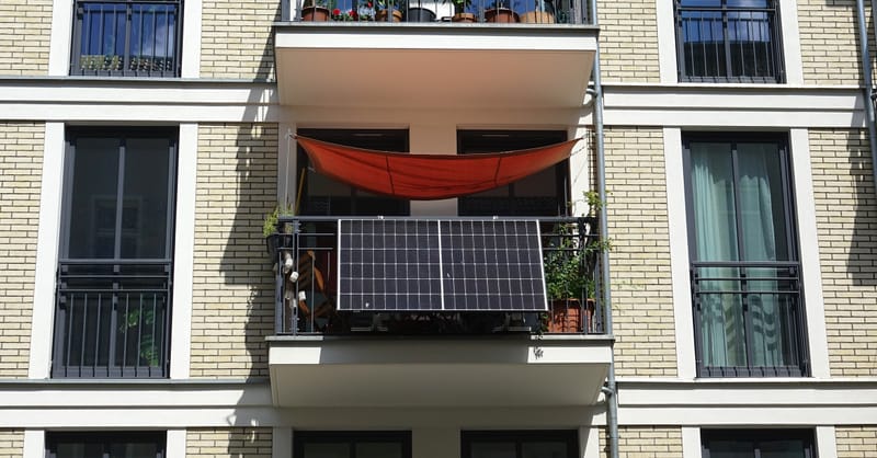 A modern apartment balcony in a European city featuring two sleek solar panels mounted on the railing.