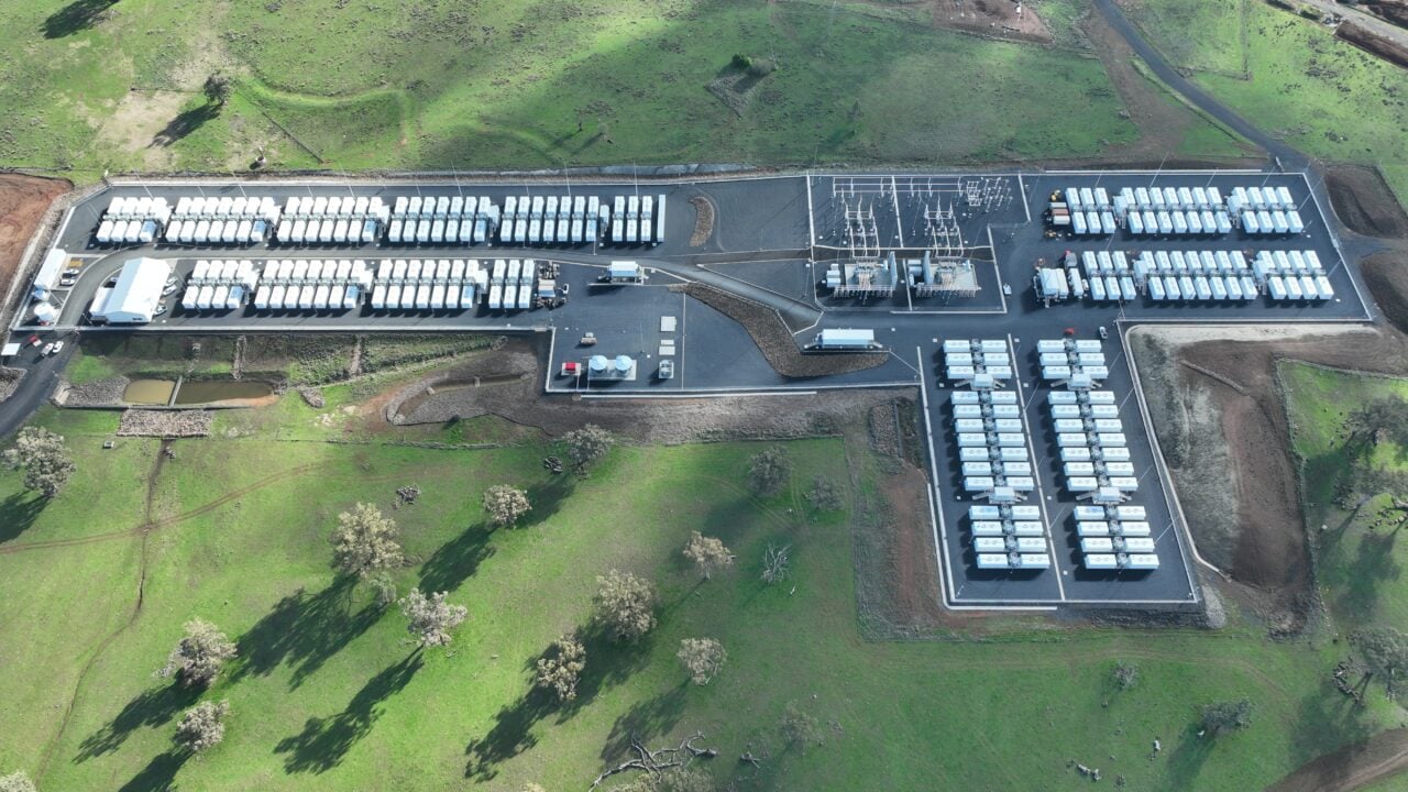 Aerial view of a massive utility-scale battery energy storage system with white containers in a grid layout.