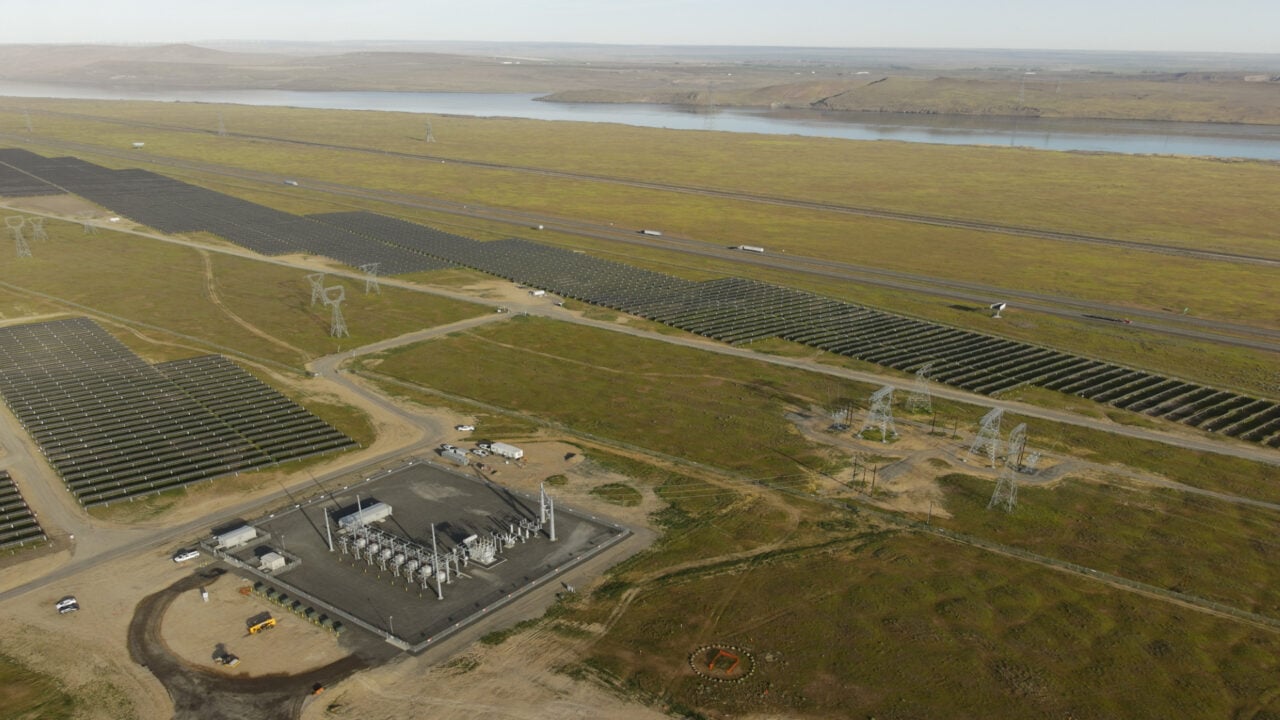 Aerial view of a massive utility-scale solar farm with thousands of blue PV panels under a clear sky.