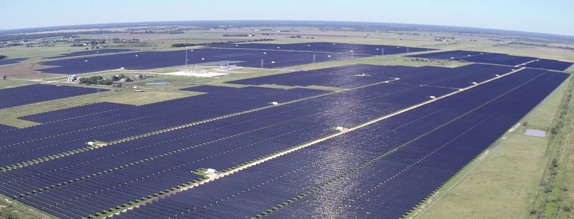 Aerial view of a massive solar array integrated with shipping-container-sized battery storage units.
