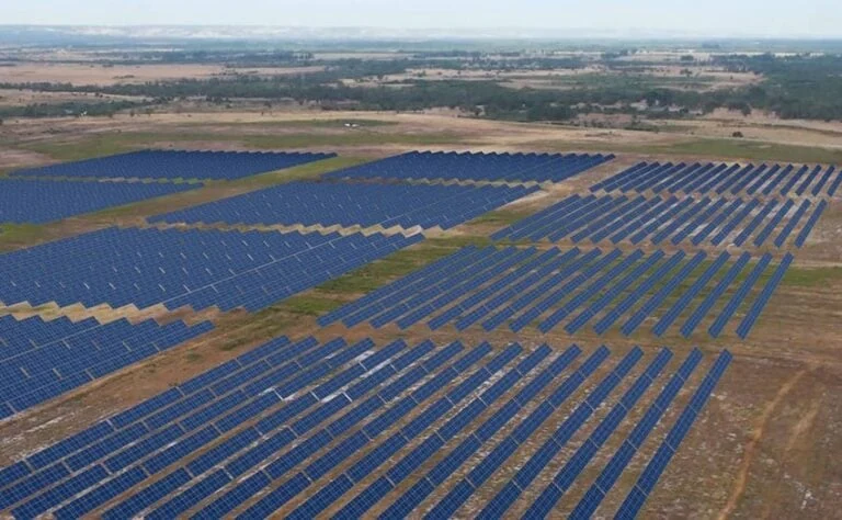 Aerial view of a large-scale solar array integrated with massive battery storage containers in a dry climate.