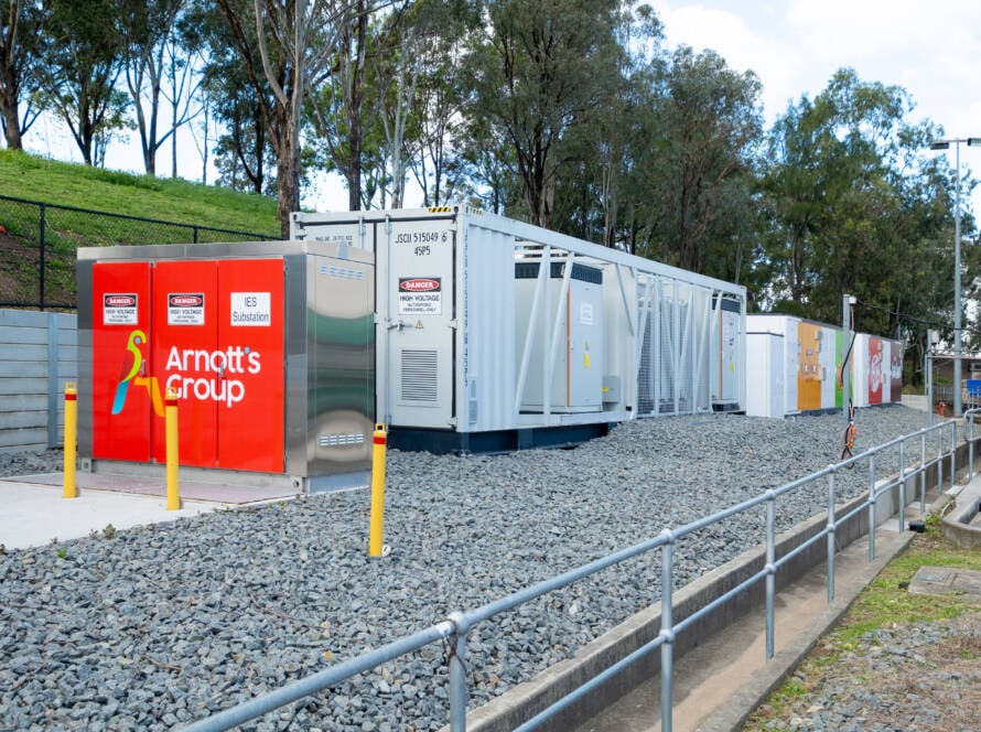 A row of industrial solar panels on a warehouse roof with a battery container.