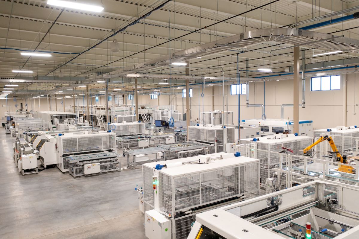 A technician inspecting solar cells in a high-tech manufacturing facility next to a residential solar installation site.