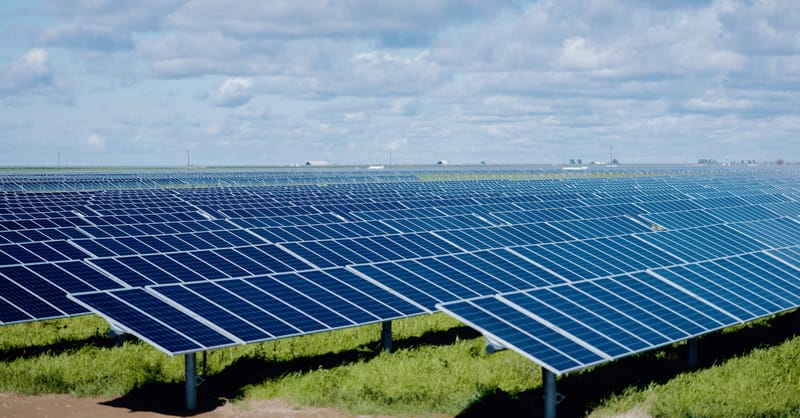 A vast expanse of solar panels installed across California agricultural land near a highway.