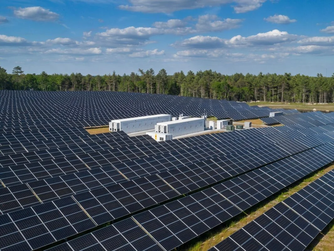 Industrial scale battery storage containers sitting next to a large solar farm at sunset.