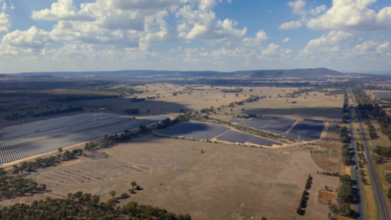A large-scale solar farm with industrial battery storage containers visible in the foreground.