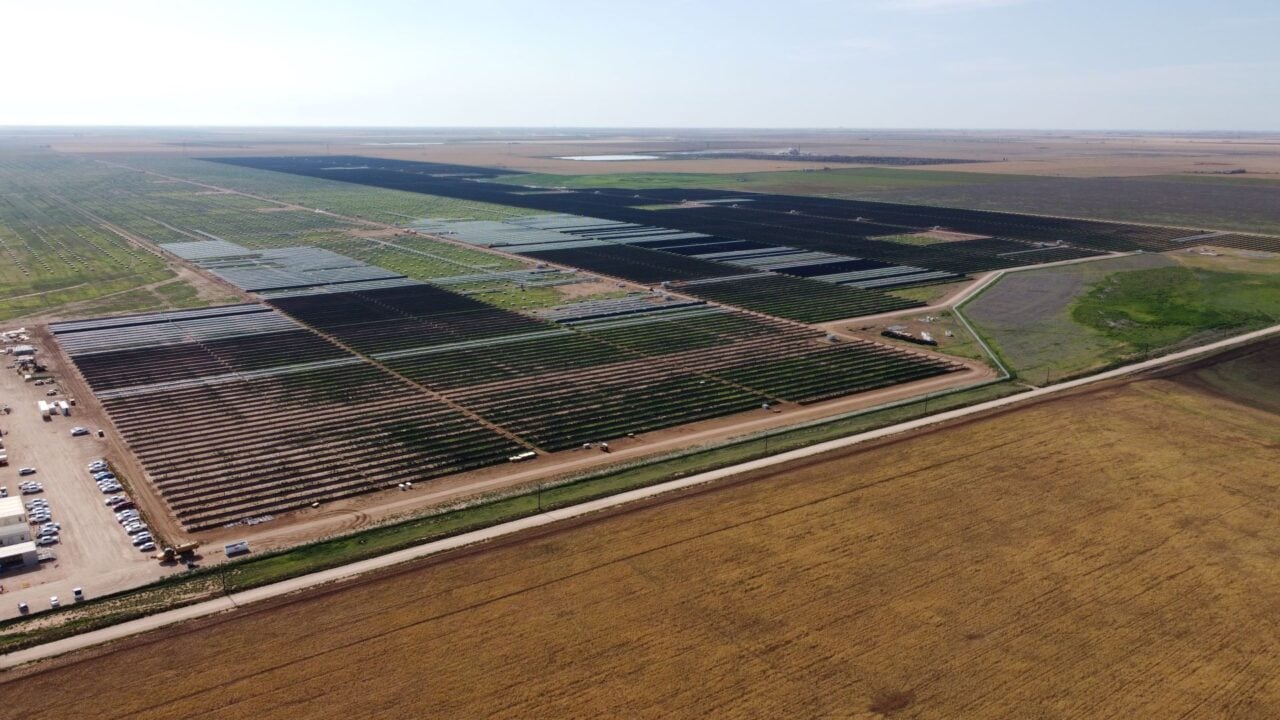 Large scale solar farm construction site with idle cranes and stacked PV modules