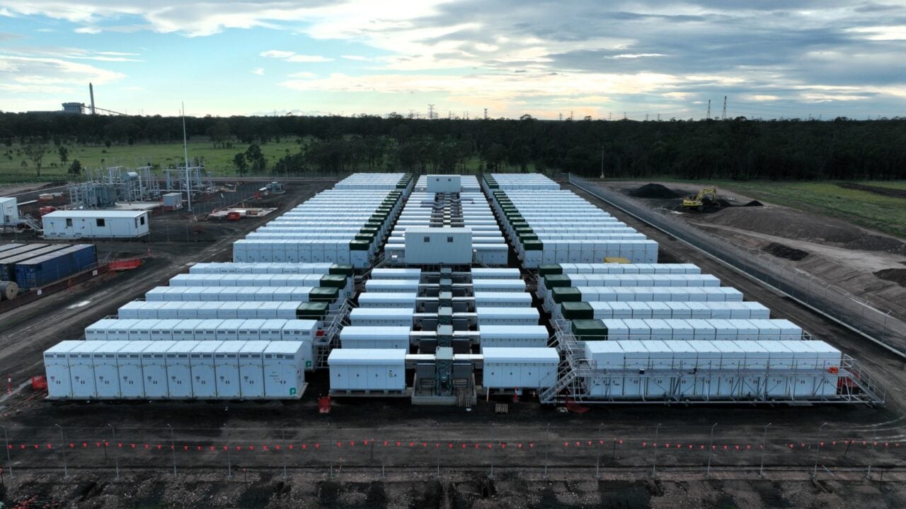 A massive containerized battery storage site during sunset in a German industrial landscape.