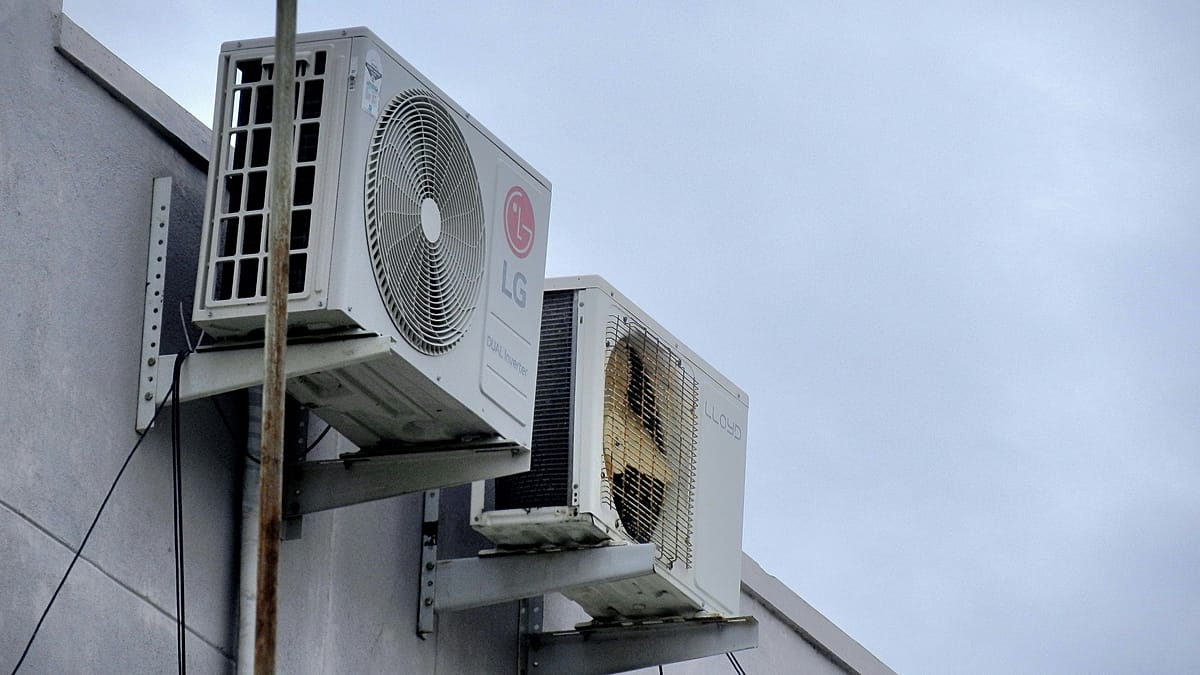 A modern air-to-water heat pump unit installed outside a European home with solar panels on the roof.