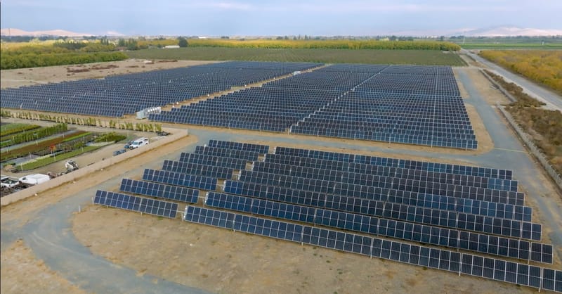 A large-scale solar farm with battery storage containers under a clear blue sky