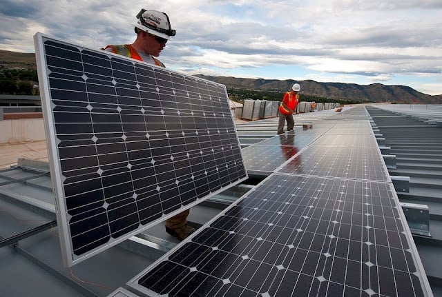 A large-scale commercial solar panel array on an industrial warehouse rooftop.