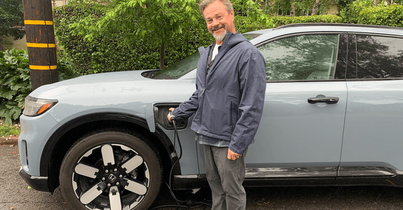 A modern residential home with solar panels installed on the roof and an electric vehicle charging in the driveway.