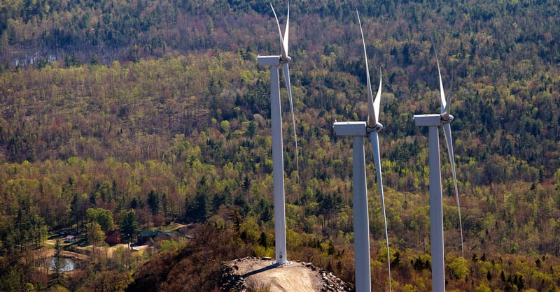 Aerial view of a wind turbine farm in a remote, forested landscape during autumn.