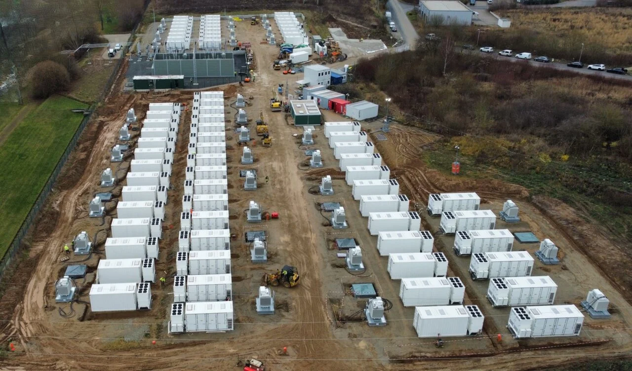 A large-scale battery energy storage container in a German industrial park at dusk.