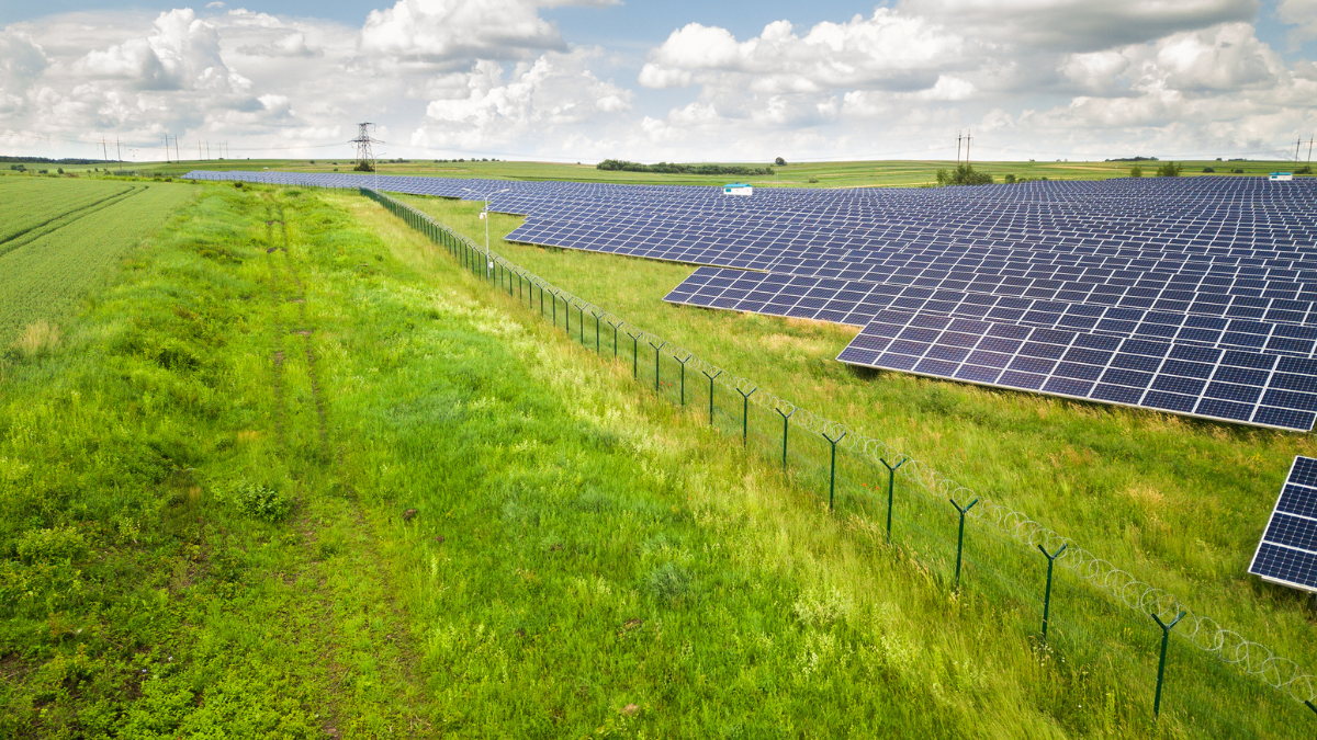 Aerial view of a massive solar PV array installed on rolling green hills under a cloudy sky.