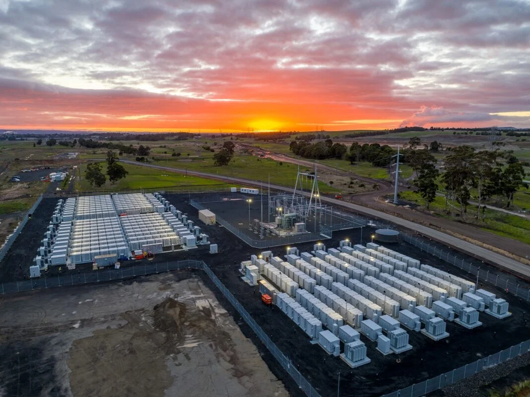 Aerial view of a massive solar farm integrated with shipping-container-sized battery storage units in a rural landscape.