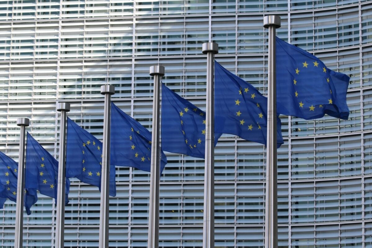 A close-up of a solar panel being installed with the EU flag in the background blurred.