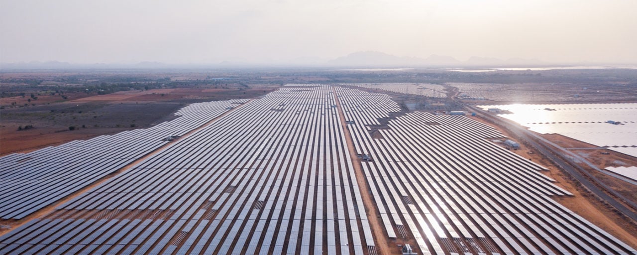 A large-scale solar farm under construction with rows of solar panels extending to the horizon