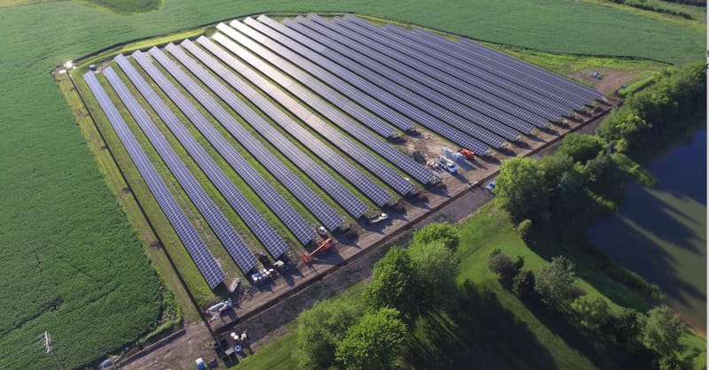 A technician inspecting a large-scale community solar array under a clear blue sky