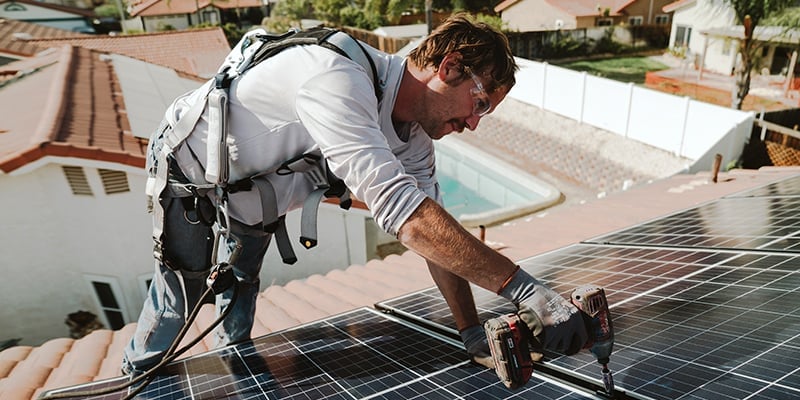 A row of residential rooftop solar panels under a cloudy sky.