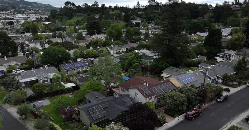Modern suburban homes with solar panels and battery storage units forming a distributed energy network.