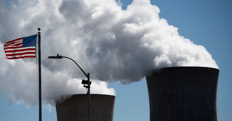 A modern nuclear power plant cooling tower standing next to a field of solar panels.