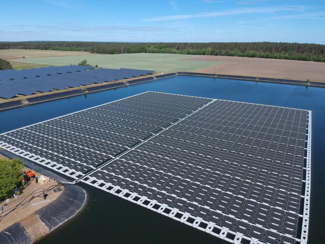Floating solar array on a calm reservoir with technical mooring systems visible below the waterline.